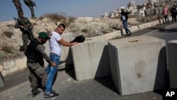FILE - Israeli border police search a Palestinian next to newly placed concrete blocks in an East Jerusalem neighborhood, Oct. 15, 2015.