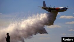 A television reporter stands in front of a Large Air Tanker (LAT) C-130 Hercules, also known as ‘Thor,’ as it drops a load of around 15,000 liters of retardant during a display ahead of the bushfire season, at RAAF Base Richmond, Sydney, Australia, Sept. 1, 2017.