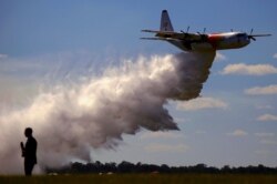 Seorang reporter televisi berdiri di depan Large Air Tanker (LAT) C-130 Hercules, juga dikenal sebagai 'Thor', saat menjatuhkan beban sekitar 15.000 liter selama pameran oleh Dinas Pemadam Kebakaran Pedesaan menjelang musim kebakaran di RAAF Pangkalan Richmond Sydney. (Foto: Reuters)