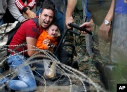 A migrant man holding a boy react as they are stuck between Macedonian riot police officers and migrants during a clash near the border train station of Idomeni, northern Greece, as they wait to be allowed by the Macedonian police to cross the border from