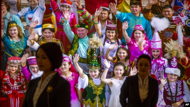 FILE - Tour guides stand in front of a large photo depicting different ethnic groups in Xinjiang at the Exhibition of the Fight Against Terrorism and Extremism in Urumqi in northwestern China's Xinjiang Uyghur Autonomous Region, April 21, 2021.