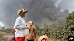 Warga desa setempat mengamati gunung Sinabung saat kembali mengeluarkan awan tebal di Namantaram, Sumatera Utara, Indonesia (1/2).