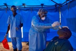 FILE - A member of South Sudanese Ministry of Health's Rapid Response Team takes a sample from a man who has recently been in contact with a confirmed case of the COVID-19 coronavirus in Juba, South Sudan, April 13, 2020.