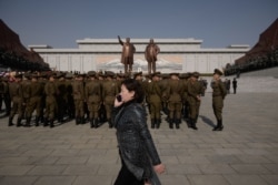 FILE - A woman talks on a mobile phone as Korean People's Army soldiers gather for a memorial tribute before the statues of late North Korean leaders Kim Il Sung and Kim Jong Il, on Mansu hill in Pyongyang, North Korea, April 15, 2019.
