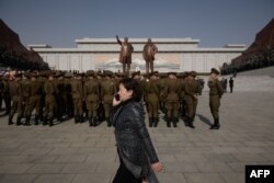 FILE - A woman talks on a mobile phone as Korean People's Army soldiers gather for a memorial tribute before the statues of late North Korean leaders Kim Il Sung and Kim Jong Il, on Mansu hill in Pyongyang, North Korea, April 15, 2019.