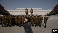 FILE - A woman talks on a mobile phone as Korean People's Army soldiers gather for a memorial tribute before the statues of late North Korean leaders Kim Il Sung and Kim Jong Il, on Mansu hill in Pyongyang, North Korea, April 15, 2019. 