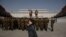 FILE - A woman talks on a mobile phone as Korean People's Army soldiers gather for a memorial tribute before the statues of late North Korean leaders Kim Il Sung and Kim Jong Il, on Mansu hill in Pyongyang, North Korea, April 15, 2019. 