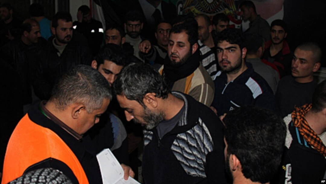 Arab league observer, left, with orange vest, writes names of freed Syrian prisoners, Damascus, Jan. 15, 2012.