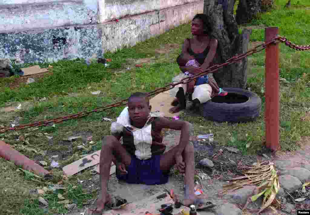 Assis devant une femme sans arbi portant un bébé, un enfant abandonné dans&nbsp; la rue répare ses chaussures de fortunes sur la bordure d&#39;une rue de Kinshasa, capitale de la République Démocratique du Congo, juin 2013. (Reuters) 