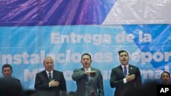 El presidente guatemalteco, Jimmy Morales, al centro, canta el himno nacional acompañado del alcalde de Mixco, Ernesto Bran, a la derecha, y el ministro de cultura, Jose Chex, durante la inauguración de un campo de fútbol en Mixco, Guatemala, el 17 de septiembre del 2018. 