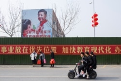 FILE - Men ride a scooter past a poster showing Chinese President Xi Jinping on the side of a school building in Henan province, China, Feb. 22, 2019.