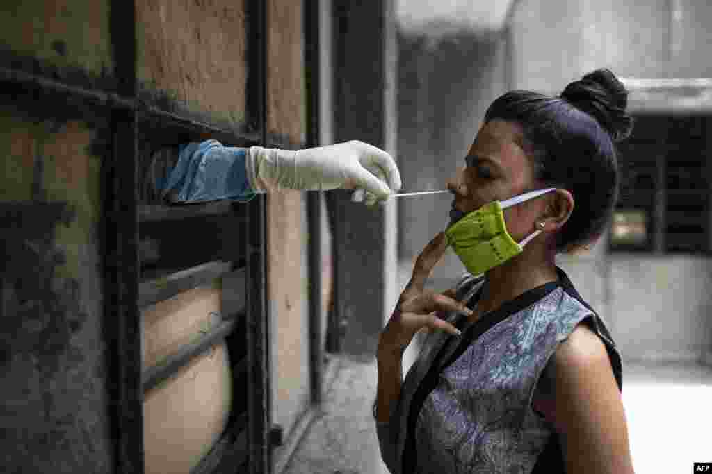 A health official, left, collects a swab sample from a woman to test for the COVID-19 coronavirus at a temporary free testing facility set up in a school after authorities eased lockdown restrictions, in New Delhi, India.