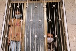Children wearing protective masks look from behind a window during a 24-hour curfew amid concerns about the spread of the coronavirus disease (COVID-19), in Sana'a, Yemen, May 6, 2020.