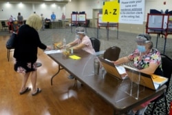 Election workers Adonlie DeRoche, seated left, and Judy Smith, seated right, assist voters during primary elections on July 14, 2020, in Portland, Maine.