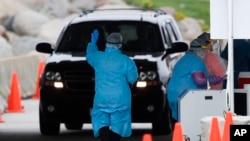 FILE - A medical worker directs a local resident at a drive-thru COVID-19 testing site in Waterloo, Iowa, May 1, 2020. 