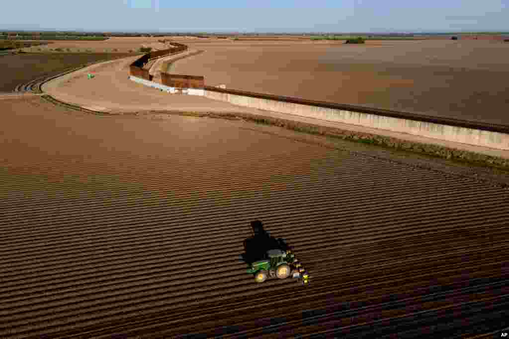 In this photo taken by a drone, the border wall construction is seen near farmland as a tractor plows a field.