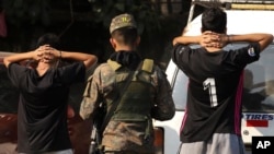 ARCHIVO - Un soldado verifica la identificación de jóvenes en la calle principal del barrio La Campanera en Soyapango, El Salvador, el 5 de marzo de 2023.