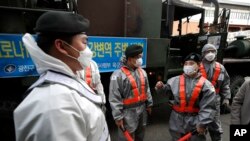 South Korean soldiers in protective gear talk as they disinfect on the street as a precaution against the new coronavirus in Seoul, South Korea, March 12, 2020. 