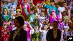 FILE - Tour guides stand in front of a large photo depicting different ethnic groups in Xinjiang at the Exhibition of the Fight Against Terrorism and Extremism in Urumqi in northwestern China's Xinjiang Uyghur Autonomous Region, April 21, 2021. 