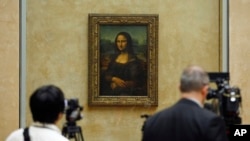 Members of the media are gathered next to the Mona Lisa, during an event to unveil the new lighting of Leonardo da Vinci's painting Mona Lisa earlier this year. The Mona Lisa is famous for her enigmatic smile.
