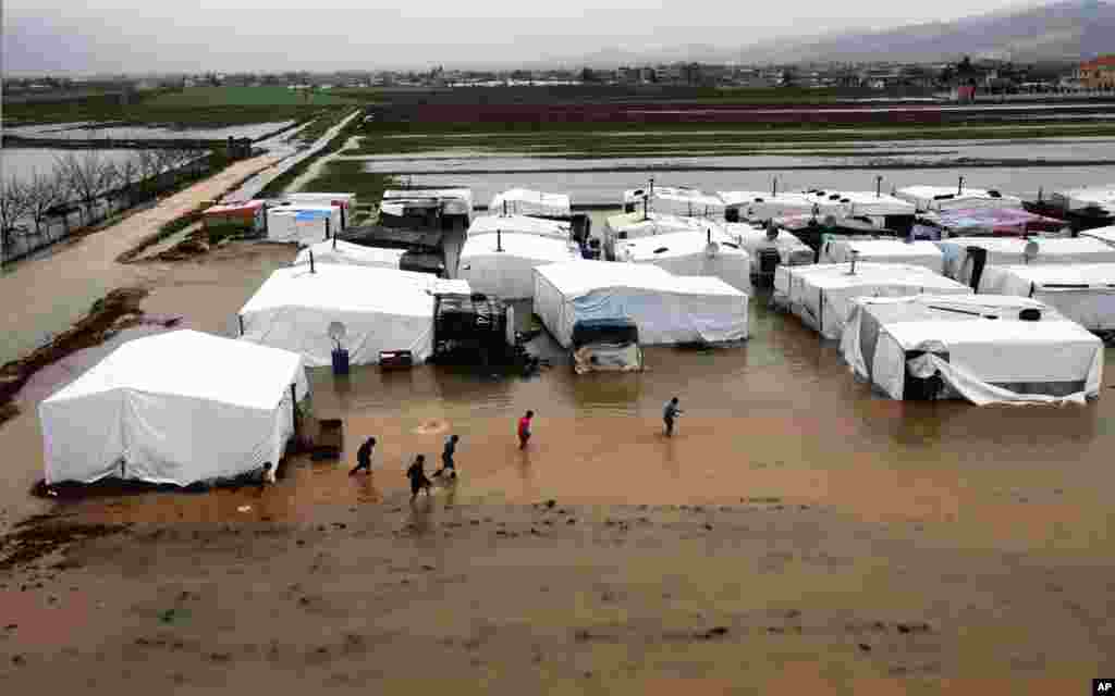 Syrian refugees make their way through a flooded temporary camp in Al-Faour, Lebanon, near the border with Syria.