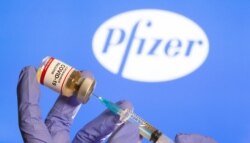 FILE PHOTO: A woman holds a small bottle labeled with a "Coronavirus COVID-19 Vaccine" sticker and a medical syringe in front of displayed Pfizer logo.