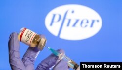 FILE PHOTO: A woman holds a small bottle labeled with a "Coronavirus COVID-19 Vaccine" sticker and a medical syringe in front of displayed Pfizer logo.