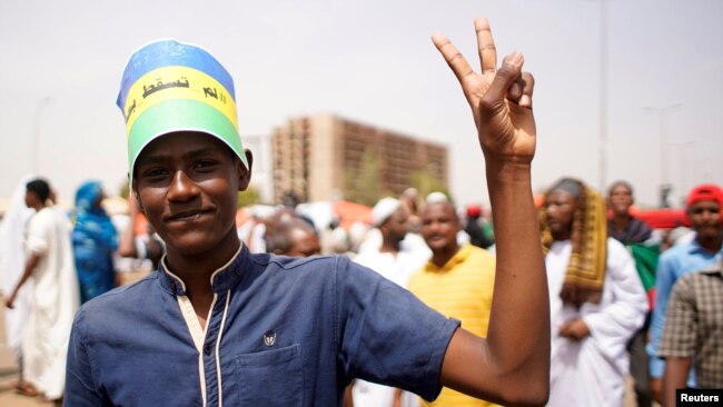 FILE - A Sudanese demonstrator flashes victory sign during a protest against the army's announcement that President Omar al-Bashir would be replaced by a military-led transitional council, in Khartoum, Sudan, April 12, 2019. 