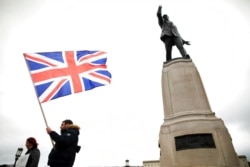 FILE - Loyalist protesters opposed to the Northern Ireland Protocol on Brexit make their point under the statue of former Unionist leader Lord Edward Carson at Stormont, Belfast, Northern Ireland, April 8, 2021.