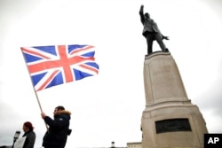 FILE - Loyalist protesters opposed to the Northern Ireland Protocol on Brexit make their point under the statue of former Unionist leader Lord Edward Carson at Stormont, Belfast, Northern Ireland, April 8, 2021.