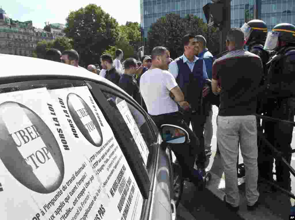 Les chauffeurs de taxi en grève parlent aux agents de police d'émeute à côté d'une cabine avec des affiches portant la mention "Stop Uber, hors la loi", lors d'une manifestation de chauffeurs de taxi à Paris, France, le 25 juin, 2015