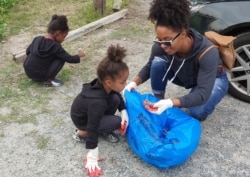 A family picks up trash along the banks of the Potomac River in Alexandria, Virginia, during a cleanup day sponsored by the Potomac Riverkeeper Network. (Deborah Block/VOA)