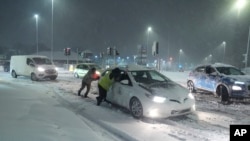 Sejumlah warga tampak mendorong mobil yang terjebak di jalanan bersalju di Leeds, Inggris, pada 5 Januari 2025. (Foto: Danny Lawson/PA via AP)