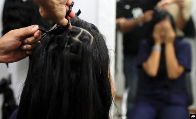 Valery Díaz covers her face as she gets her hair cut off for $100 at a beauty salon in Caracas, Venezuela, April 5, 2019.