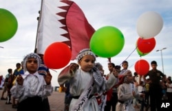 FILE- Palestinian children wave balloons and Qatari flags while waiting for the convoy of the Emir of Qatar, not pictured, to pass by a street in Gaza City, Oct. 23, 2012. A diplomatic standoff between Qatar and a quartet of Arab nations accusing it of sponsoring terrorism has thrust a spotlight on an opaque network of charities and prominent figures freely operating in Qatar, as well as individuals once embraced by leaders across the Gulf.