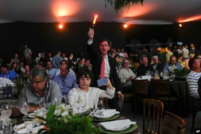 A spotter waves a light stick to signal receipt of a new bid at the Elo de Raça auction in Uberaba, Minas Gerais state, Brazil, Sunday, April 28, 2024. The Elo de Raça is the most prestigious auction at the world’s biggest Zebu fair. (AP Photo/Silvia Izquierdo)