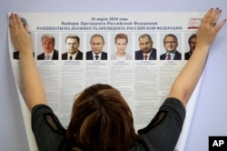 FILE - A polling station employee hangs a list of candidates for the 2018 Russian presidential election during preparations for the election at a polling station in St.Petersburg, Russia, March 16, 2018.