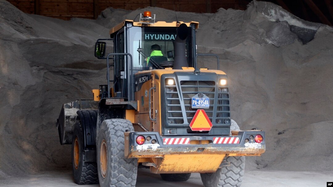 A worker at a Pennsylvania Department of Transportation maintenance area in Franklin Park, Pa., along Interstate 79 north of Pittsburgh, uses heavy machinery to move road treatment material from storage to load onto trucks, March 13, 2017.