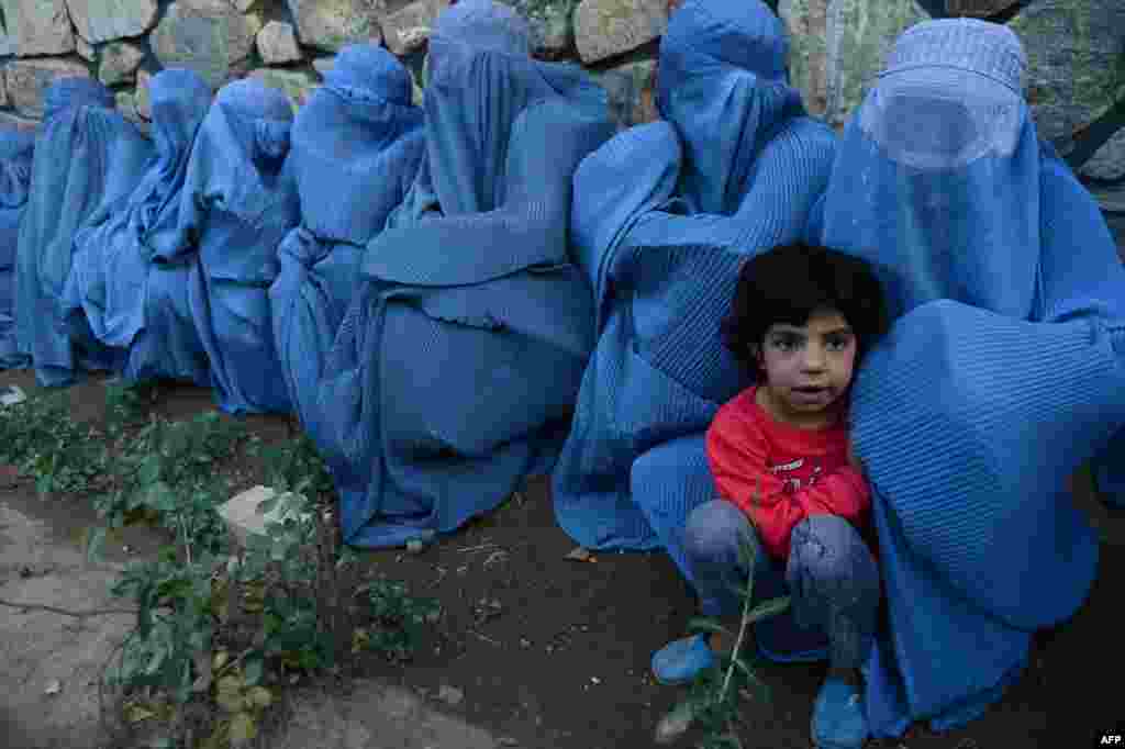 Afghan women and a child wait for food from distribution during Ramadan in Herat, June 23, 2015.