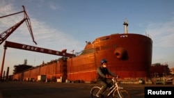 2011年11月13日，中國南方城市廣州，一名工人騎著自行車經過中國船舶工業集團龍穴造船公司一艘即將完工的船。