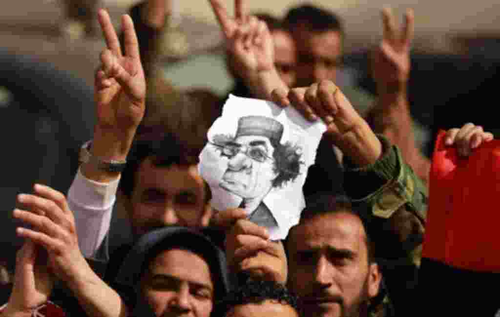 Libyan protesters flash the V for "victory" sign and hold a caricature of leader Moamer Kadhafi during a rally in the eastern city of Tobruk on February 24, 2011 as residents of Libya's dissident-held east, frenzied by a deadly crackdown by Kadhafi's crum