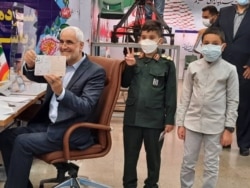 آقای مهرعلیزاده در روز ثبت نام برای انتخابات با دو نوه خود حضور یافت که یکی از این کودکان، لباس سپاه به تن داشت. عکس: رسانه‌های ایران