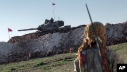 FILE - A Syrian Kurdish militia member of the YPG patrols near a Turkish army tank as Turks work to build a new Ottoman tomb in the background in Esme village in Aleppo province, Syria, Feb. 22, 2015.