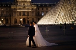 Pasangan pengantin baru melewati Museum Louvre yang sepi pengunjung di Paris Jumat (30/10), di tengah penerapan PSBB nasional untuk mengatasi lonjakan Covid-19 di Perancis.