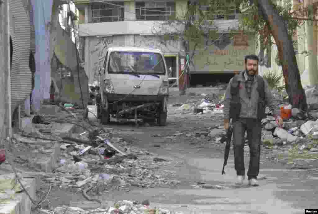 A Free Syrian Army fighter holds his weapon as he walks along a damaged street in the besieged area of Homs, Jan. 30, 2014. 