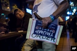 An Israeli man holds a sign of U.S. presidential candidate Republican Donald Trump as he watches a live update with friends of the U.S. presidential election results at Mike's place bar in Jerusalem, Wednesday Nov. 9, 2016.