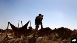 FILE - In this Sept. 26, 2014 file photo, a Kurdish Peshmerga fighter uses binoculars to check on Islamic State group's positions on the outskirts of Makhmour, 300 kilometers (186 miles) north of Baghdad, Iraq. 