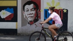 A woman wearing a protective mask rides her bicycle past an image of Philippine President Rodrigo Duterte in Manila, Philippines on Friday March 20, 2020. The Philippines is indefinitely banning the entry of foreigners after the government declared…
