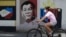 FILE - A woman wearing a protective mask rides her bicycle past an image of Philippine President Rodrigo Duterte in Manila, Philippines, on March 20, 2020. 