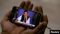 FILE - A journalist poses with a cellphone displaying Imran Khan, Prime Minister of Pakistan, speaking to the nation in his first televised address, in Karachi, Pakistan, Aug. 19, 2018.